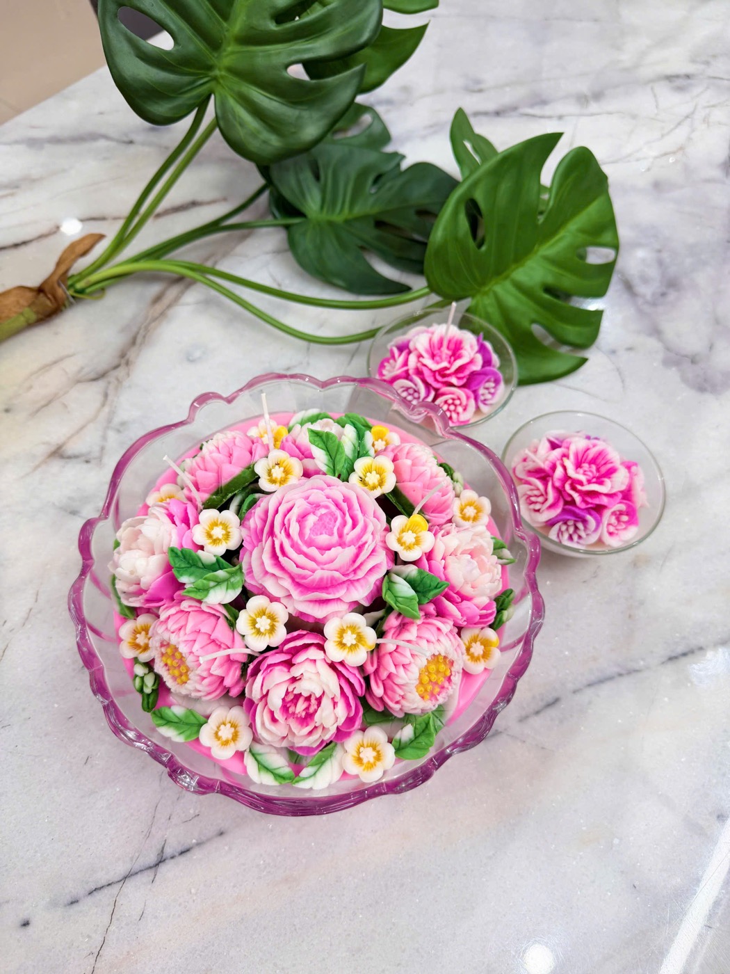 Bát nến mẫu đơn hồng nhiều tầng cánh đặt trên bàn đá hoa cương, bên cạnh hai ly nến nhỏ cùng tông